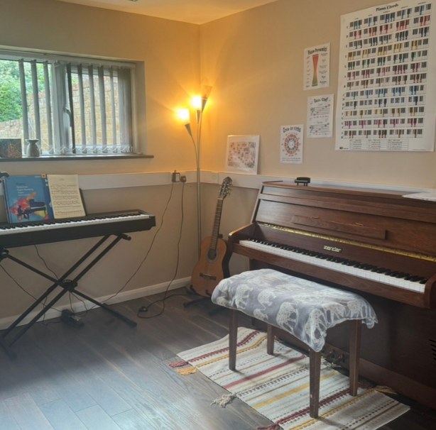 Holly's piano teaching room, with an upright piano, keyboard, guitar and music theory charts on the wall